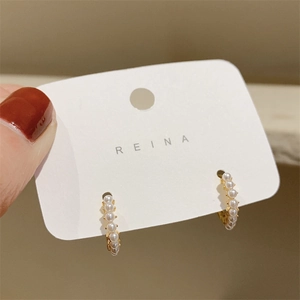 Macro detail of gold-plated hoop earrings with small white pearls on a white display card