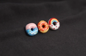 Detailed macro shot of three 3D resin cartoon donut brooches on dark fabric