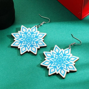 Detailed view of blue and white snowflake earrings on rustic wood with festive green background