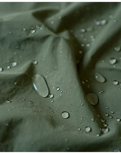 Close-up of waterproof army green fabric with water droplets showing splash resistance