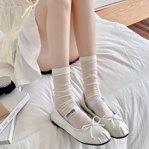White ballet flats with bow detail and ribbed cotton mid-calf socks on a cozy bed