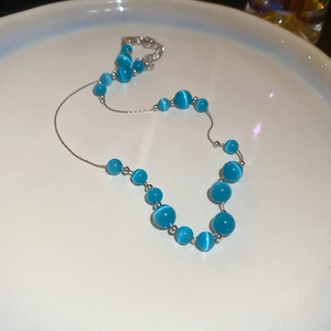 Detailed top view of blue cat-eye stone beads necklace on a white porcelain plate