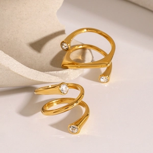 Golden spiral stainless steel ring with zircon stones on a light stone textured surface