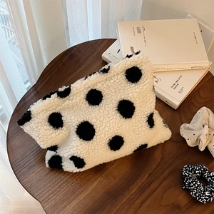 Detailed close-up of fluffy polka dot cosmetic bag with matching hair scrunchie on wood table