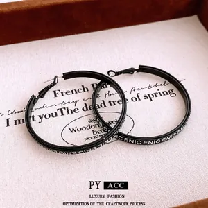 Minimalist black hoop earrings with white letter print on a textured background