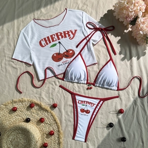 Flat lay of three-piece white bikini set with cherry print and mesh cover-up top