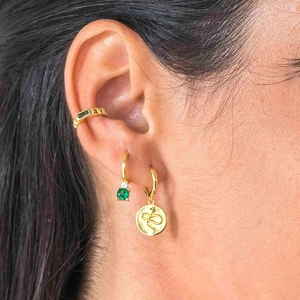 Close-up of gold-plated earrings featuring green gemstones and a snake relief charm