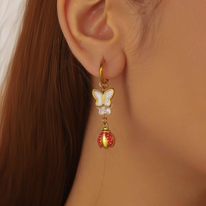 Gold hoop earrings with red ladybug and white butterfly charms shown on a model