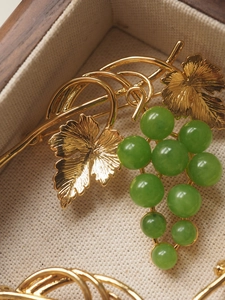 Close-up of golden grape brooch with green beads in a beige lined wooden jewelry box