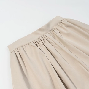 Detailed close-up of pleated beige skirt waistline with clean stitching and premium texture