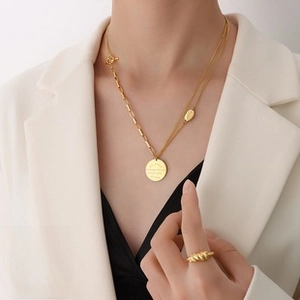 Detail of double-layer gold plated necklace with engraved round pendant and rope ring