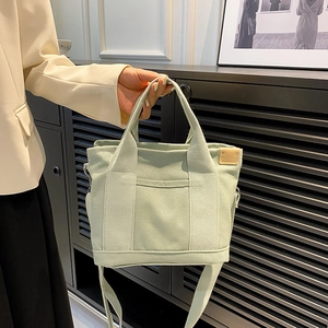 Light green minimalist canvas tote bag with shoulder strap and front pocket detail