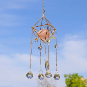 Golden geometric crystal suncatcher with pink quartz and moon charms against a blue sky