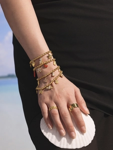 Goldene Armbänder mit Zirkonia-Anhängern und Ringen am Handgelenk eines Models am Meer