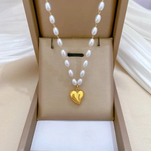 Detail of a white pearl necklace featuring a gold heart pendant in a beige jewelry box