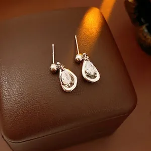 Sparkling pear-cut zircon earrings with silver posts on a premium brown leather base