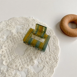 Detail view of square acetate hair claw clip with yellow green and brown stripes