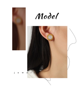 Detail view of gold gear-shaped earrings with white inlay and sparkling diamonds on model
