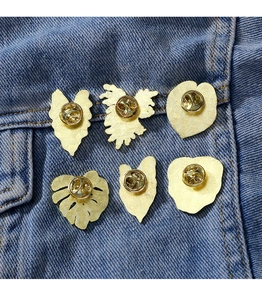 Detailed view of six golden metal tropical leaf badges pinned on a denim jacket pocket