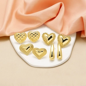 Polished gold heart and teardrop earrings set on a white ceramic tray with pink silk