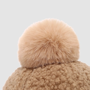 Detailed close-up of soft camel fleece texture and fluffy faux fur pompom on kid's winter hat