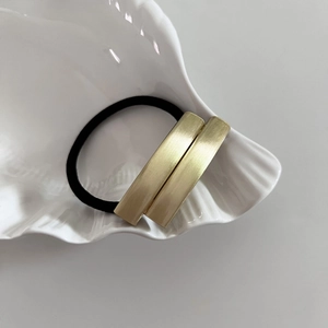 Minimalist elastic hair tie with gold brushed metal blocks on a white shell plate