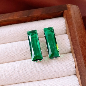 Macro shot of emerald green rectangular earrings in silver prongs on a beige fabric lining