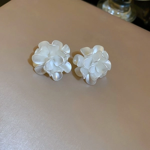 Macro view of white 3D floral stud earrings with soft pearlescent finish on matte background