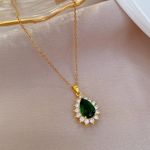 Close-up of golden teardrop emerald necklace with micro-pave crystals on beige fabric
