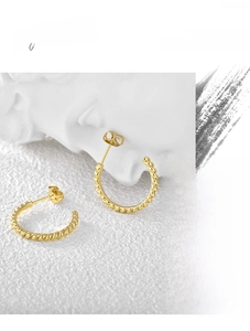 Detail shot of twisted spiral gold hoop earrings on a minimalist artistic background