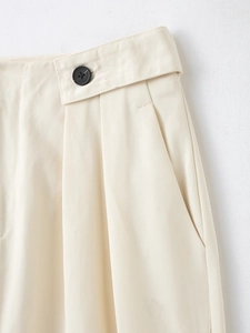 Détail de la taille haute d'un pantalon crème avec bouton noir et texture en sergé