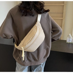 Beige woven texture crossbody bag shown from behind on a model wearing a brown hoodie