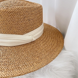 Detail of hand-woven khaki straw hat with elegant cream ribbon and fine texture