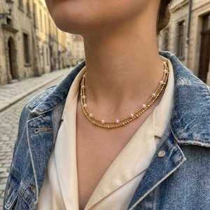 Detail of layered gold bead and freshwater pearl necklace worn on model for casual styling