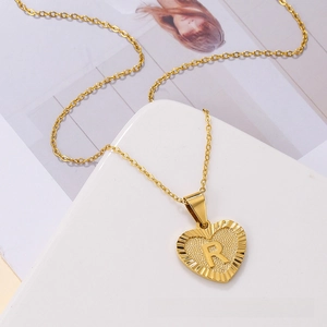 Detail of a gold heart-shaped pendant necklace featuring a central letter R and ribbed edges