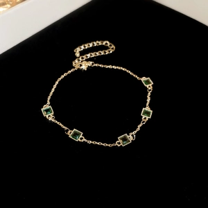 Détail d'un bracelet doré avec cinq émeraudes carrées sur fond de velours noir