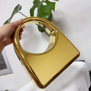 Detail of a luxury gold mirrored metal handbag with a circular handle held by hand