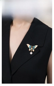Detail showing enamel butterfly brooch with blue wings and a hanging pearl on a blazer