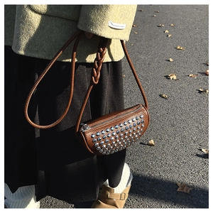 Detail of brown leather crossbody bag featuring silver punk rivets and woven strap design