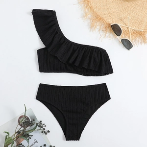 Flat lay of black one-shoulder bikini with ruffle details and summer holiday accessories