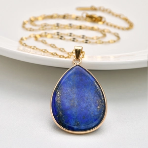 Détail d'un pendentif goutte en lapis-lazuli doré posé sur une assiette en céramique
