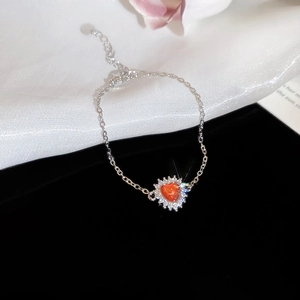Macro shot of silver heart pendant bracelet with orange gemstone and white zircon accents