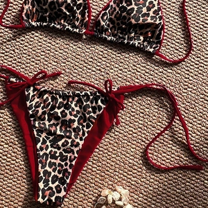 Leopard print bikini set with red trim and side ties laid on a woven mat background