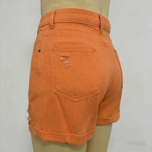 Dettaglio degli shorts di jeans arancioni a vita alta con tasca strappata e orlo risvoltato
