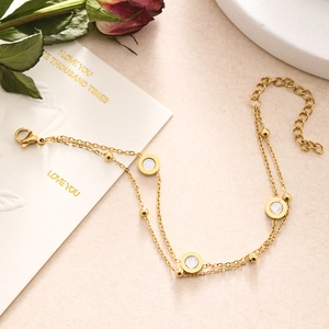 Detail of gold double-layered bracelet with mother-of-pearl charm and rose petals