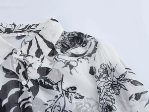 Close-up of lapel and round button on white floral chiffon shirt with black print