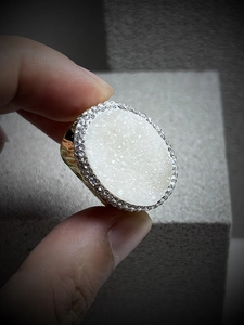 Detailed view of large white druzy crystal ring with rhinestone halo and gold-tone band