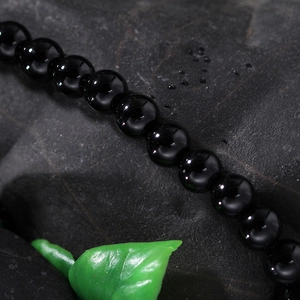Macro shot of polished black beads on textured stone with a green decorative leaf