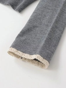 Detailed macro shot of grey knitted cardigan cuff featuring delicate beige lace stitching