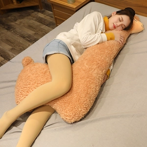 Large fluffy alpaca plush body pillow shown in a cozy bedroom sleeping scene.